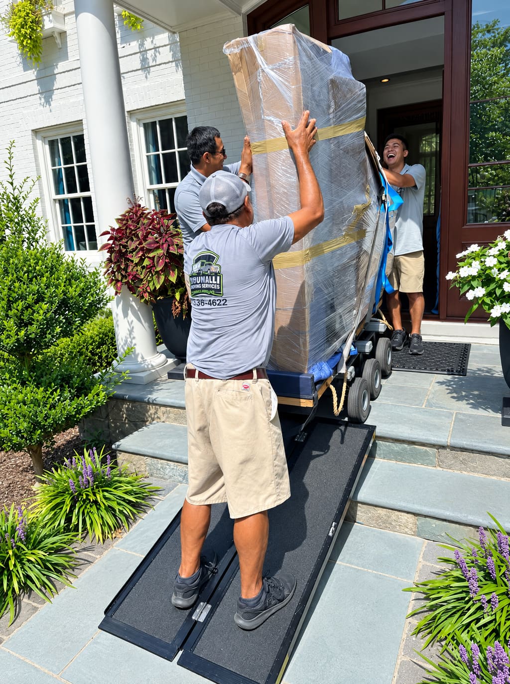 Two movers carrying a wrapped piece up the front steps on a ramp