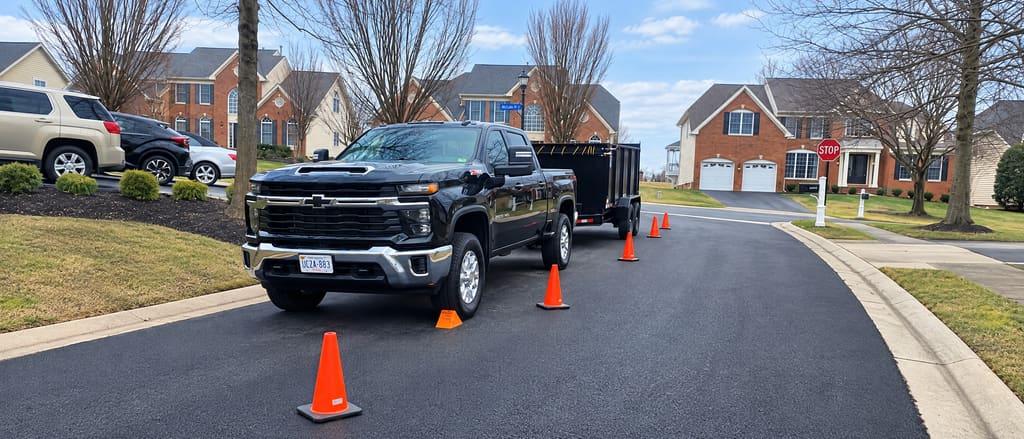 Black pickup and dump trailer on a street with cones out