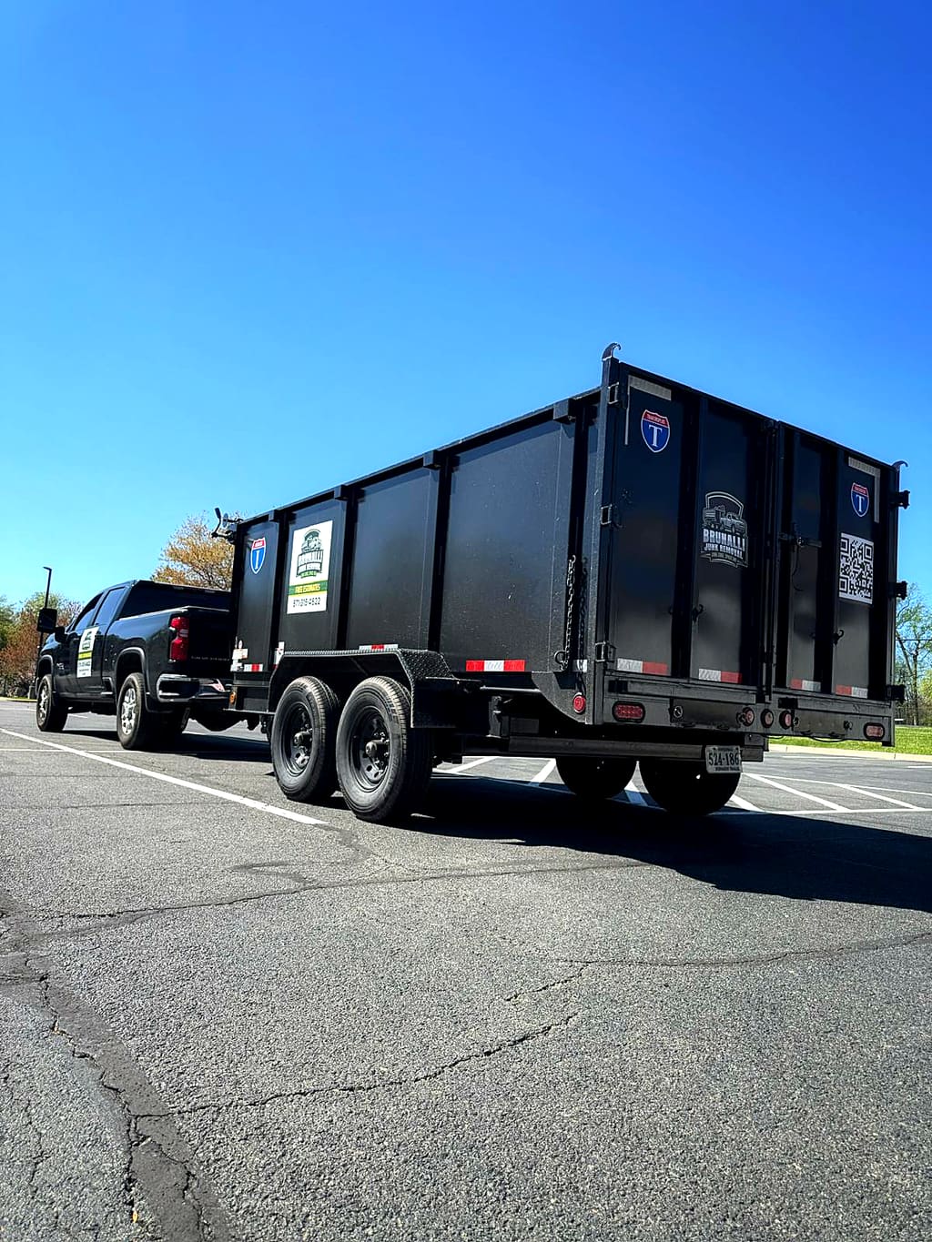 The black Brunalli dump trailer hitched to the pickup under a blue sky