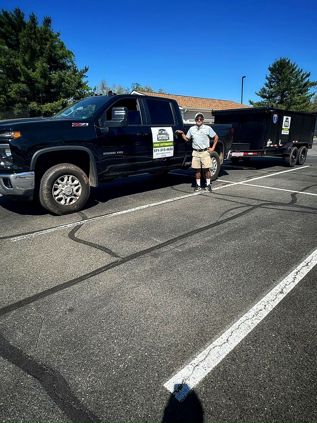 Luis standing beside the black Silverado and dump trailer with the Brunalli sign