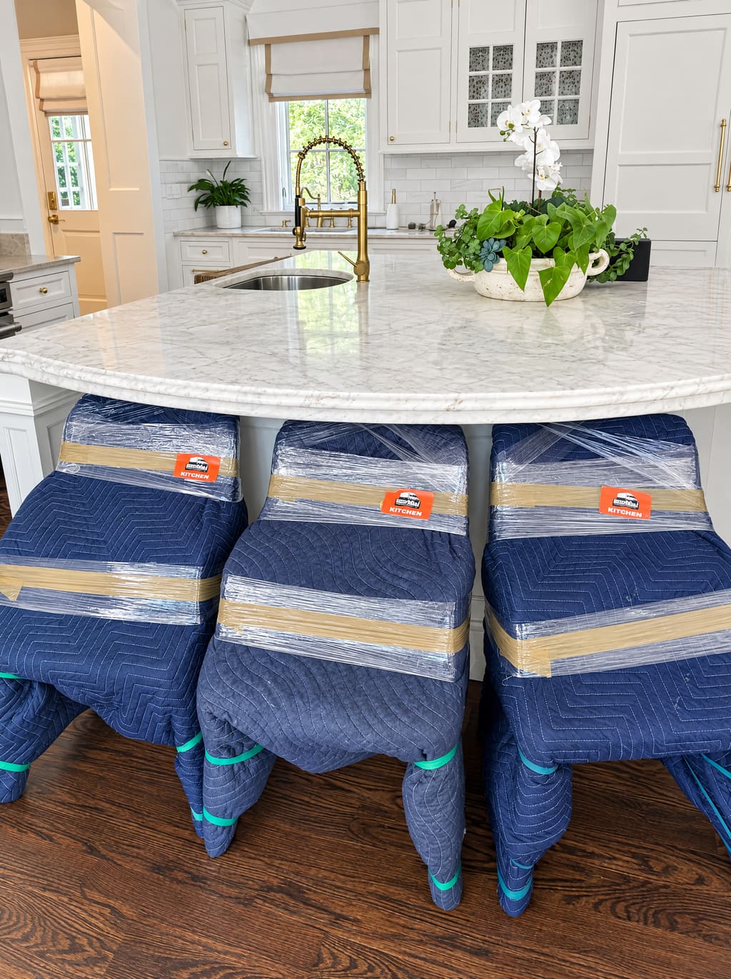 Bar stools wrapped in blue moving blankets at a marble kitchen island