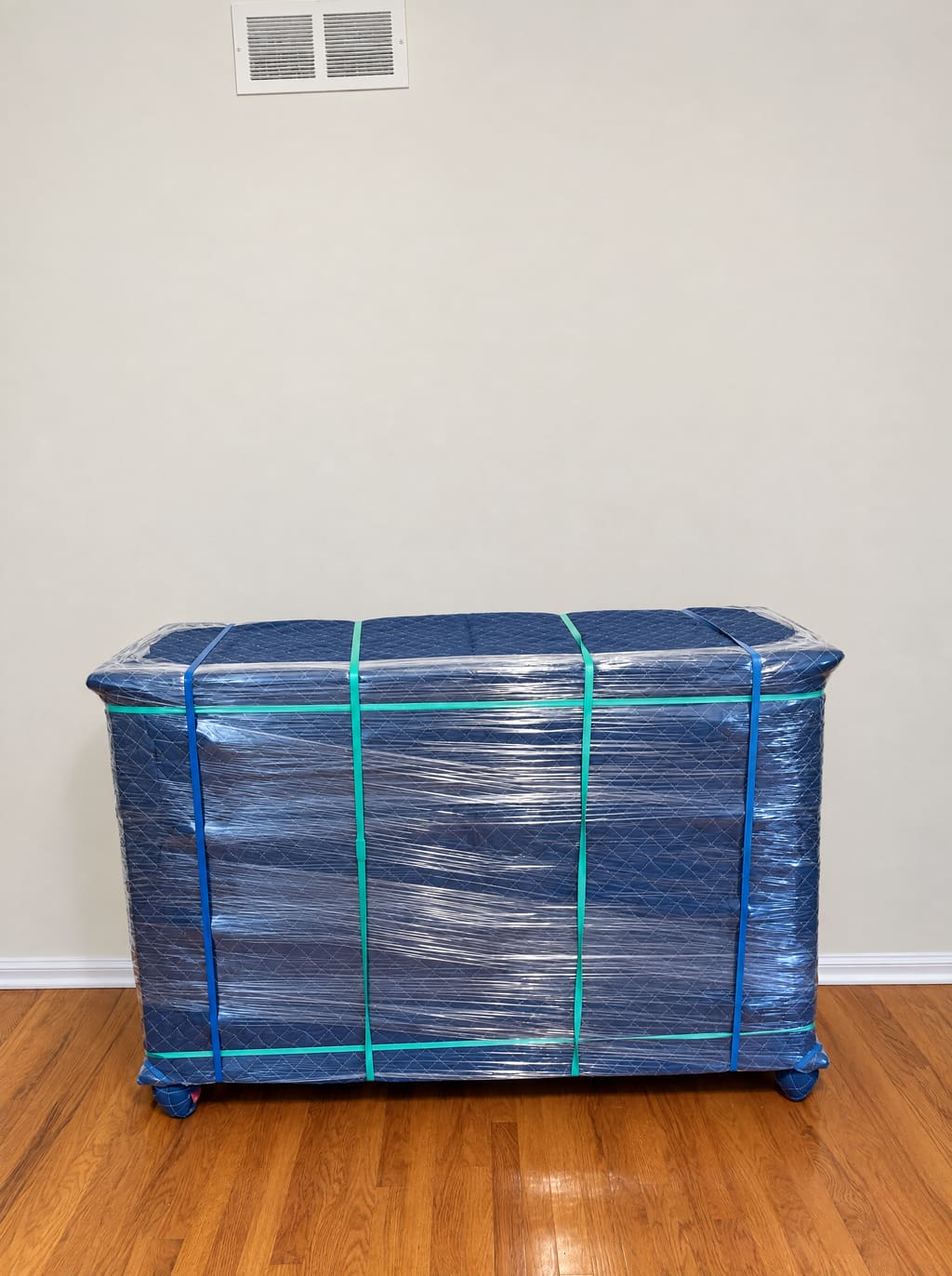 A dresser wrapped in a blue moving blanket and stretch wrap